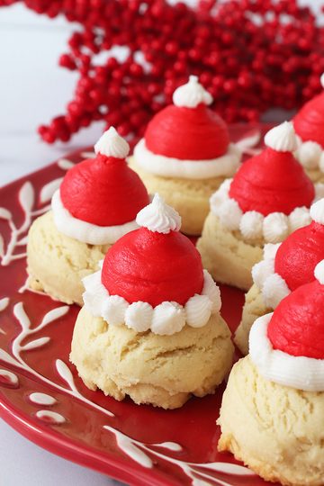 A round red plate with white embelishments topped with Santa hat drop cookies.